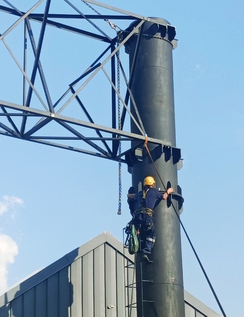 Installation of Steel Billboard Support Column (1) Technician carrying out installation work on a cylindrical steel support column for a billboard structure, with cross-braced steel framework above.